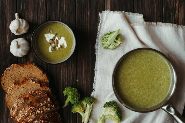 Delicious creamy broccoli soup with bread and garlic on a wooden table.