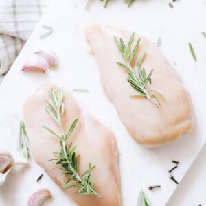 High-angle view of raw chicken breasts on marble with rosemary and garlic, ideal for healthy recipe inspiration.