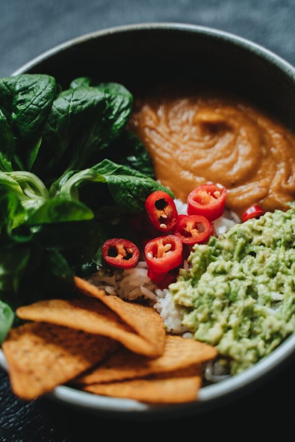 A vibrant vegan Buddha bowl featuring fresh spinach, guacamole, and chili peppers.